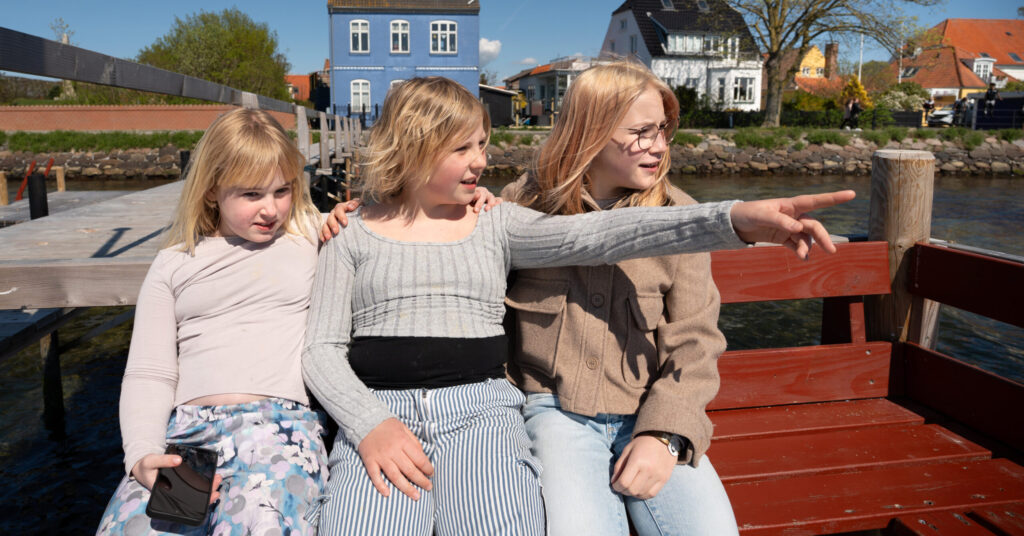 3 piger sidder på en bænk. Den midterste peger på noget.