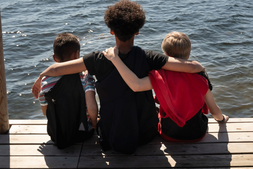 3 drenge sidder på en badebro med armene om hinanden