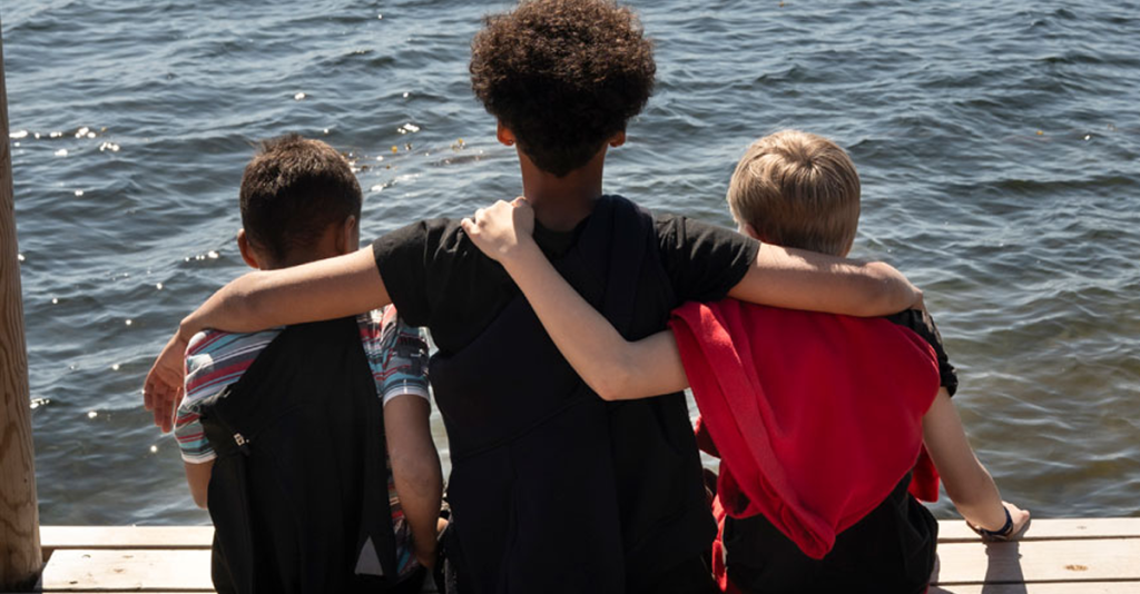 3 drenge sidder på en badebro med armene om hinanden